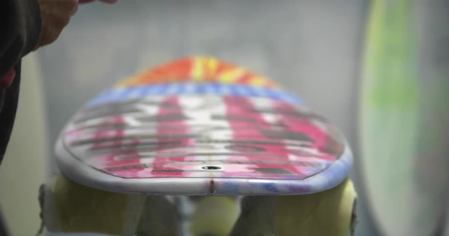 A person sanding a surfboard with an electric sander