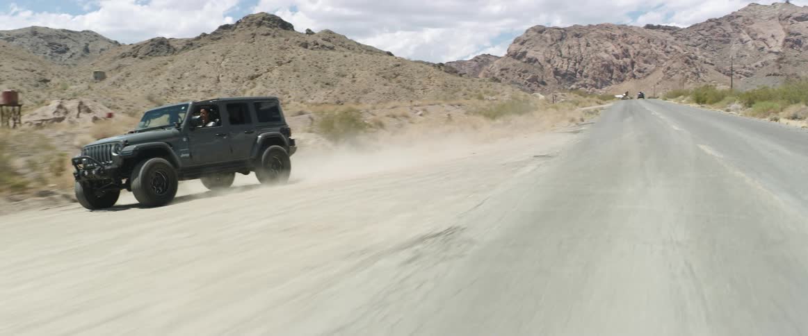 A grey jeep drives on a road in the desert and then veers off road into the dirt at daytime