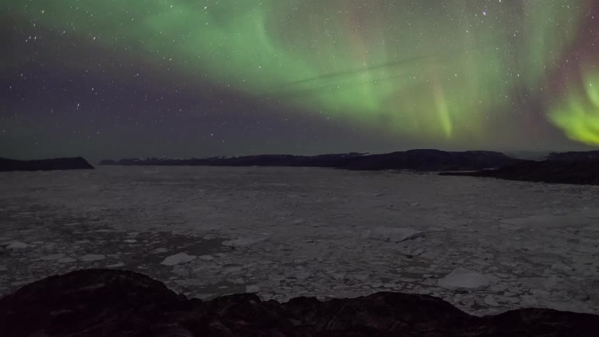 Aurora borealis shining brightly in a star filled sky above snow covered mountains and ice