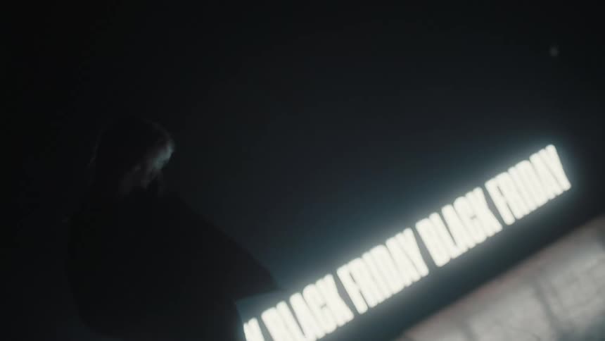 Silhouette of a woman modeling in front of a black friday sign projected on the wall of a smoky dark room