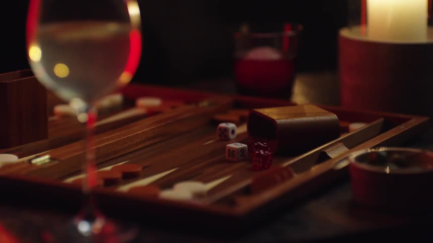 Glass of wine near a backgammon board next to a candle over a table