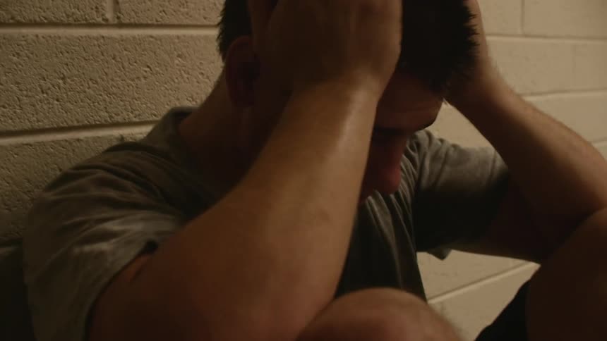Very upset man sitting against a brick wall indoors