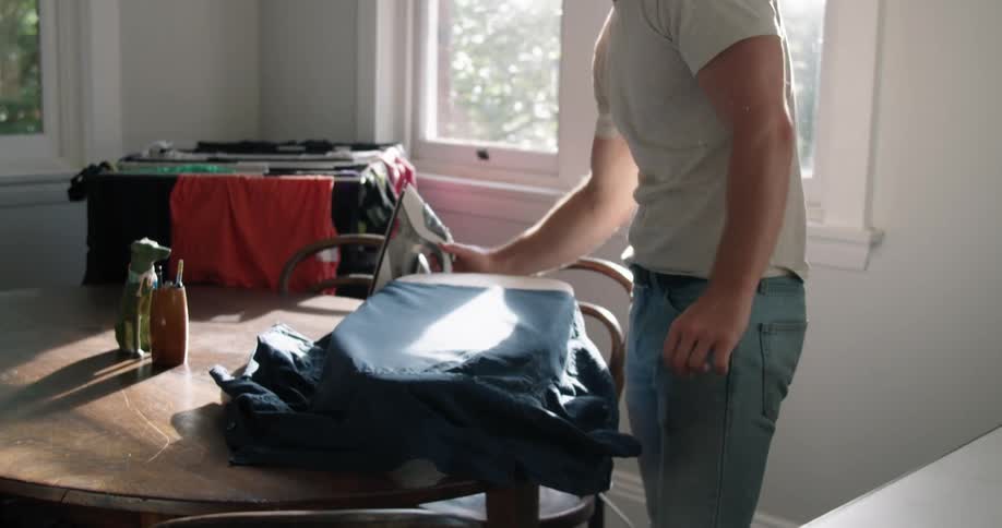 A man uses a steam iron and a tabletop ironing board to iron a shirt