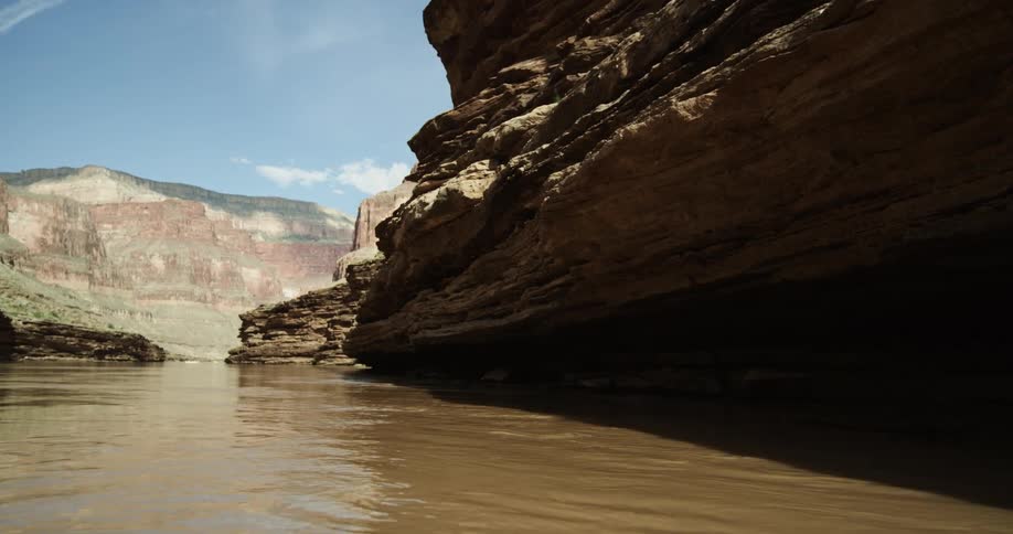 The muddy sediment filled Colorado River flows through the Grand Canyon past and underneath over hanging cliffs as experienced from a whitewater raft