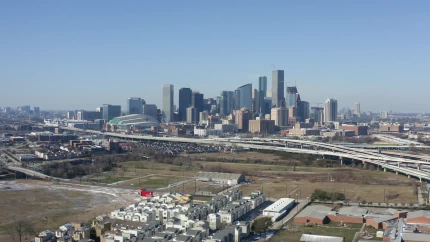 High rise buildings on the horizon from an aerial view behind a highway overpass where cars are driving below next to a small neighborhood at daytime
