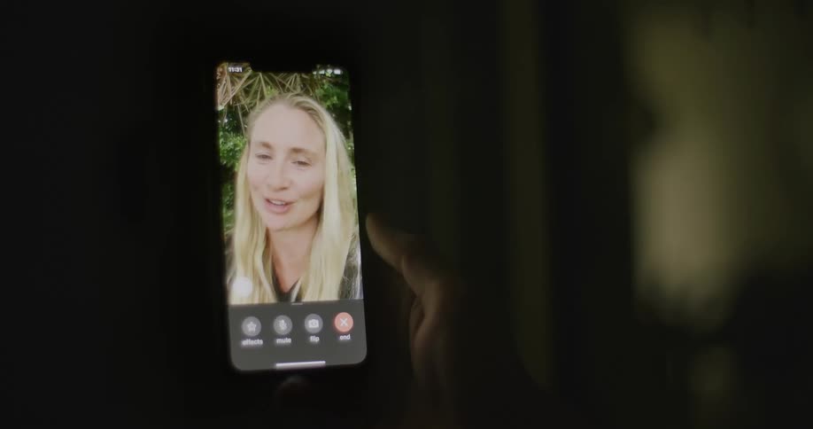 A person holds a phone with a woman on the screen as they video chat