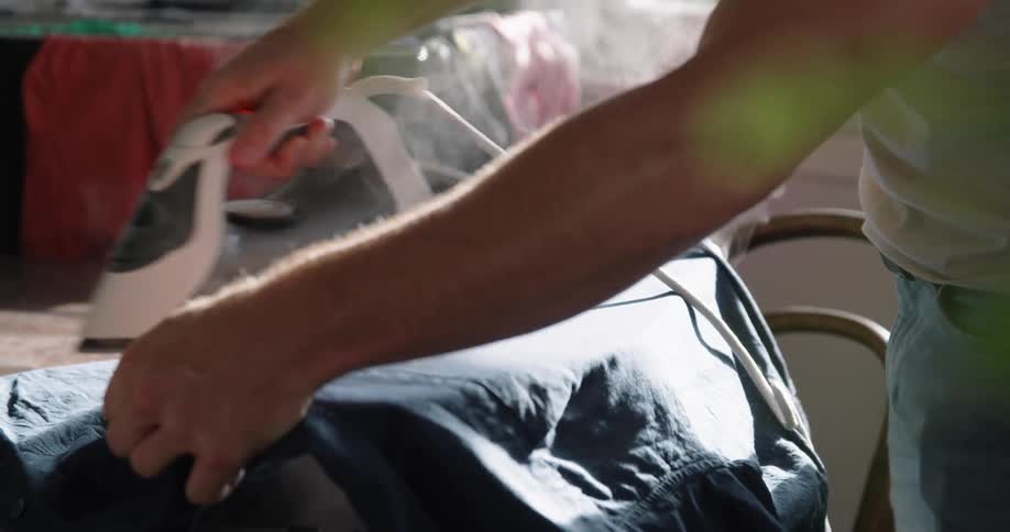 A man ironing clothes with a steaming iron over an ironing table at home