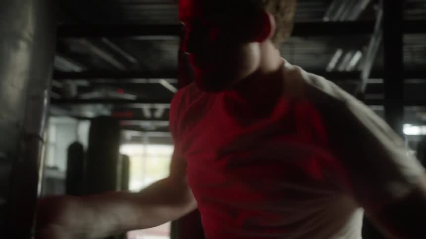 Man with white shirt and boxing gloves hits heavy bag in the boxing gym