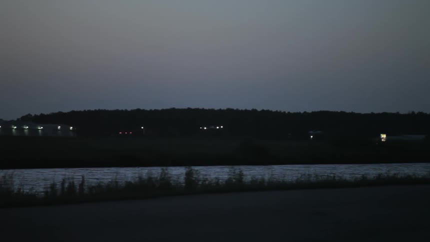 A plane slowly lands across the water at sunset