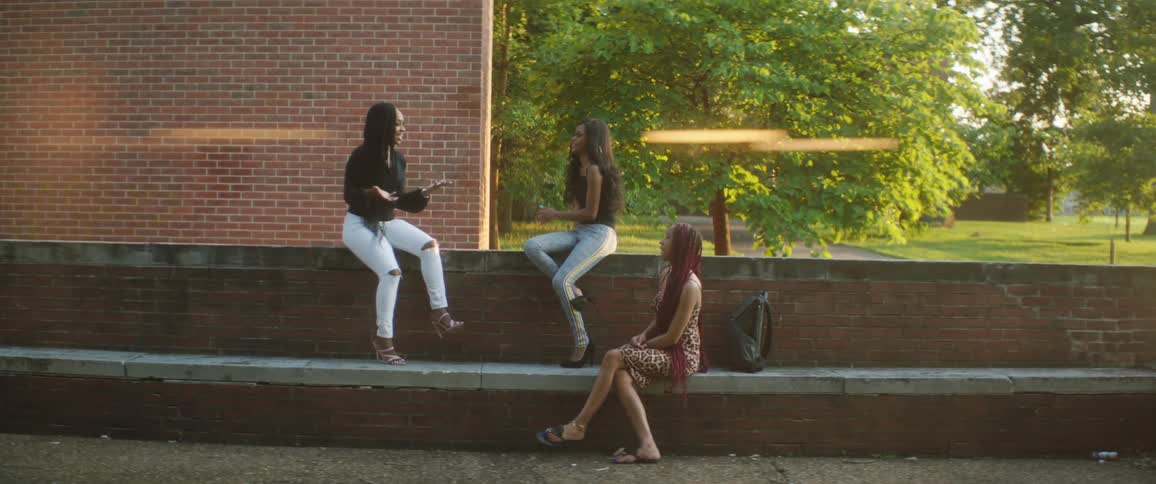 Three friends sitting on a low brick wall outside in a park chatting and smiling during the day