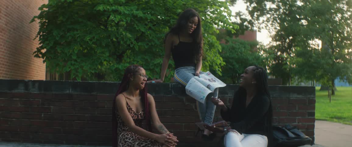 Three young women sitting outside against a brick wall in a park laughing and talking together in the evening