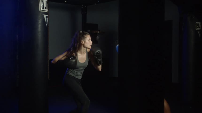 Woman with boxing gloves and black leggings trains with the couch in the boxing gym