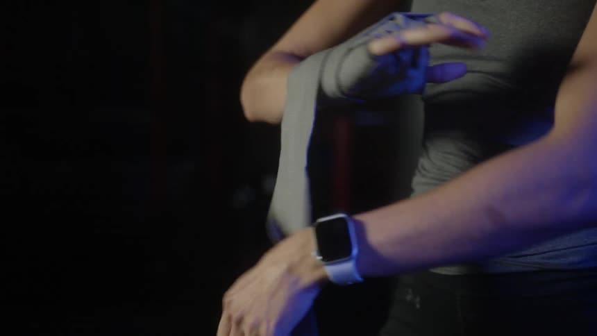 A person with a tank top and a wristwatch and ring wrapping their hand with tape