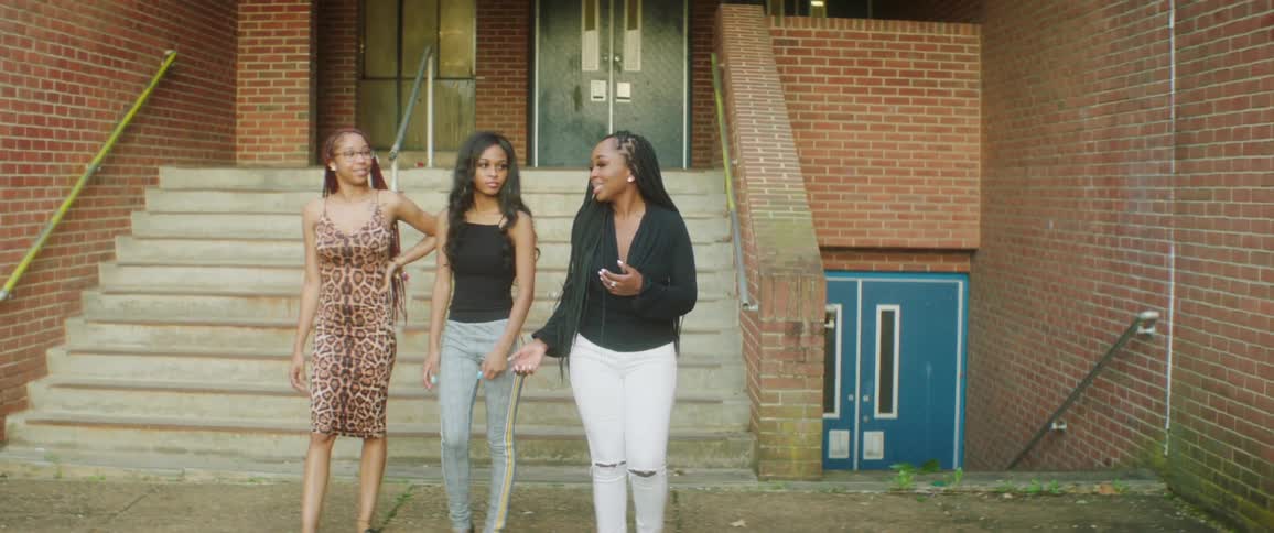 Three friends walking from the stairway of a building smiling and talking amongst one another during the day