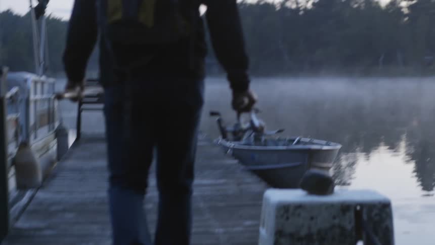 A man carrying fishing poles walks toward a boat at a dock
