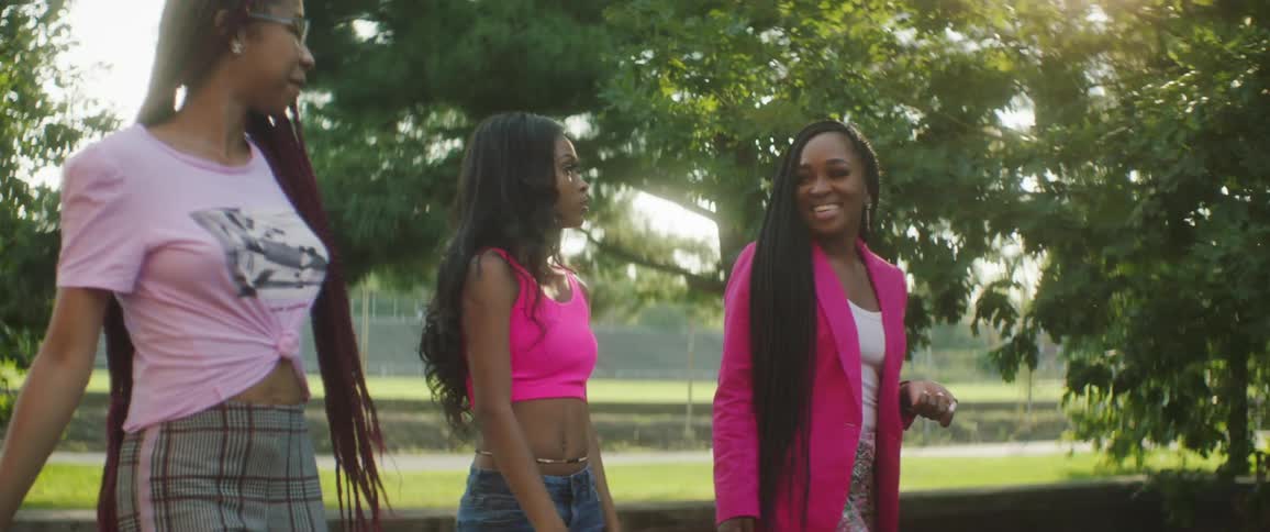Three girlfriends walk through a park on a bright sunny day