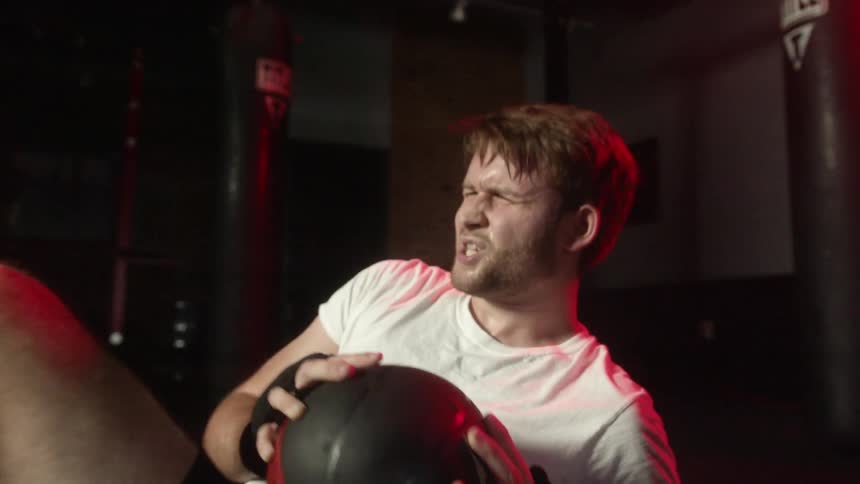 A man in a gym working out with a medicine ball surrounded by heavy bags