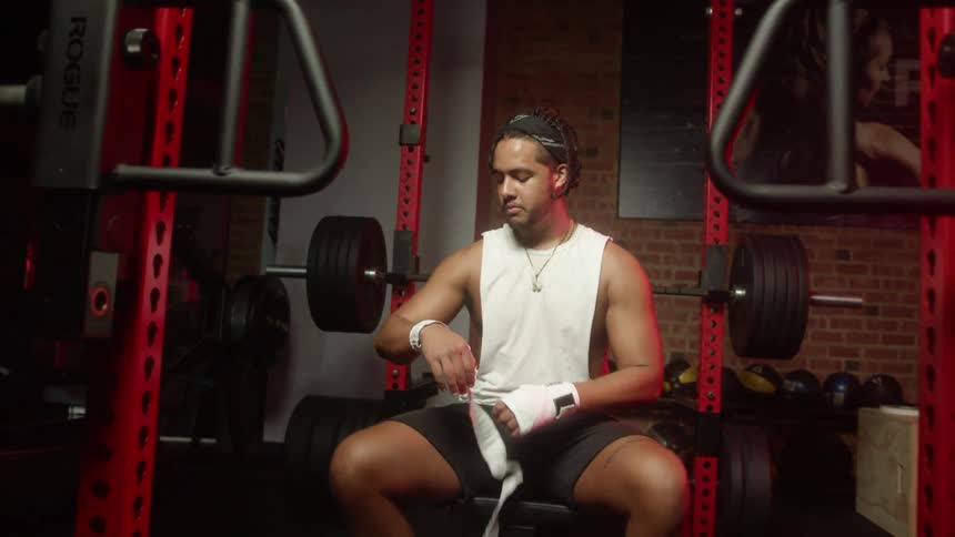 Strong muscular man wrapping his hands with white cloth bandages in a gym