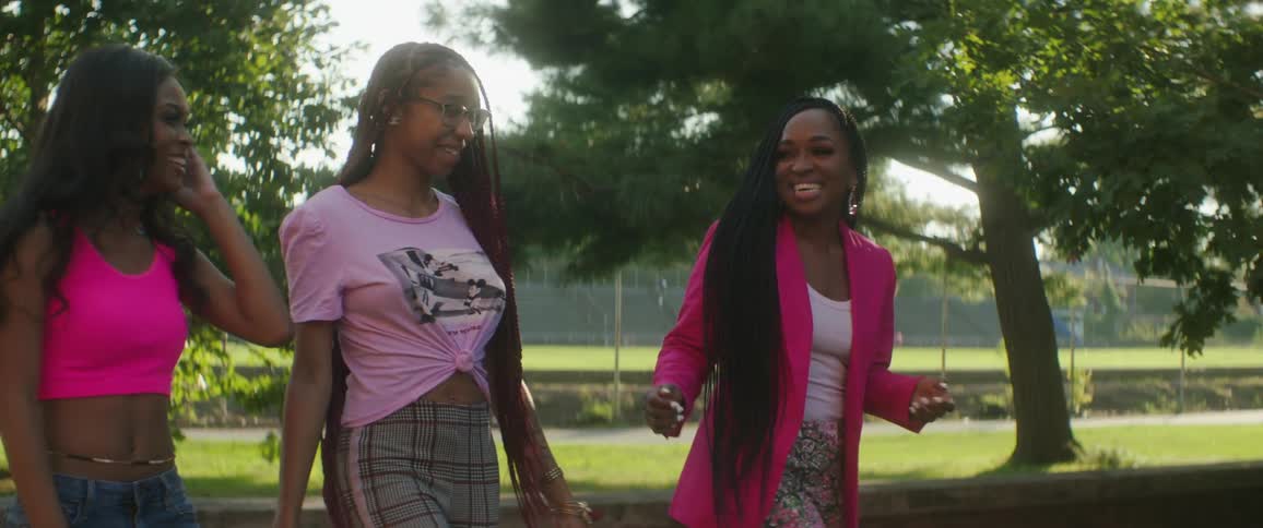 Woman touches anothers long braids as they walk smiling through park