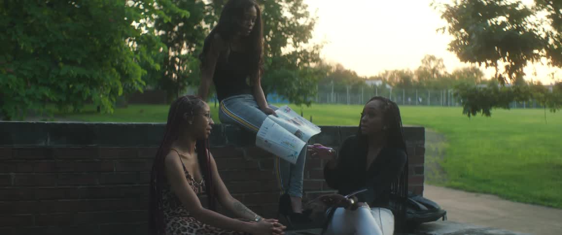 Three friends chatting while sitting outside on a low brick wall in a park at sunset