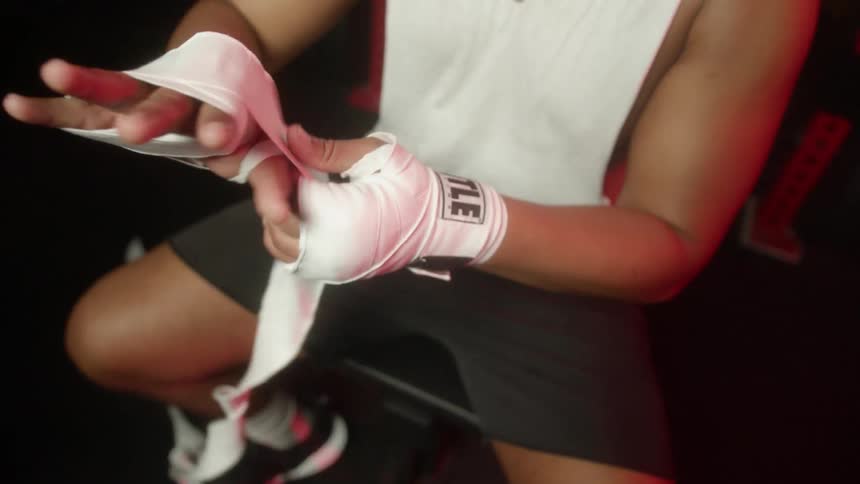 A boxer sits on a stool and wraps his right hand with white medical tape
