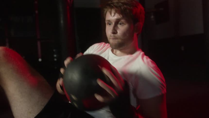 Young strong muscular man working out with a weighted ball on the floor of a gym