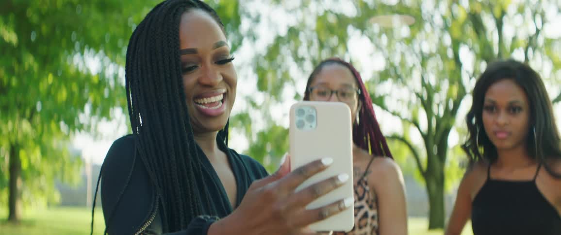 Woman and her friends standing outside in a park while she takes a selfie photo with her smart phone