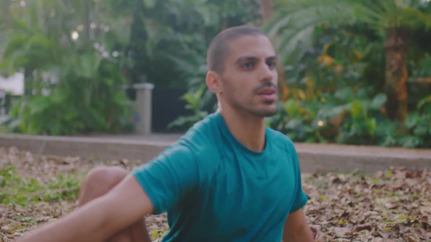 Man stretches on leave covered ground while another person walks past in background