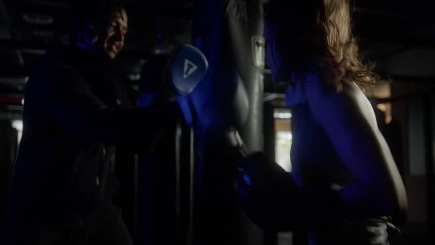 Female boxer with wavy hair trains with the coach in the boxing gym