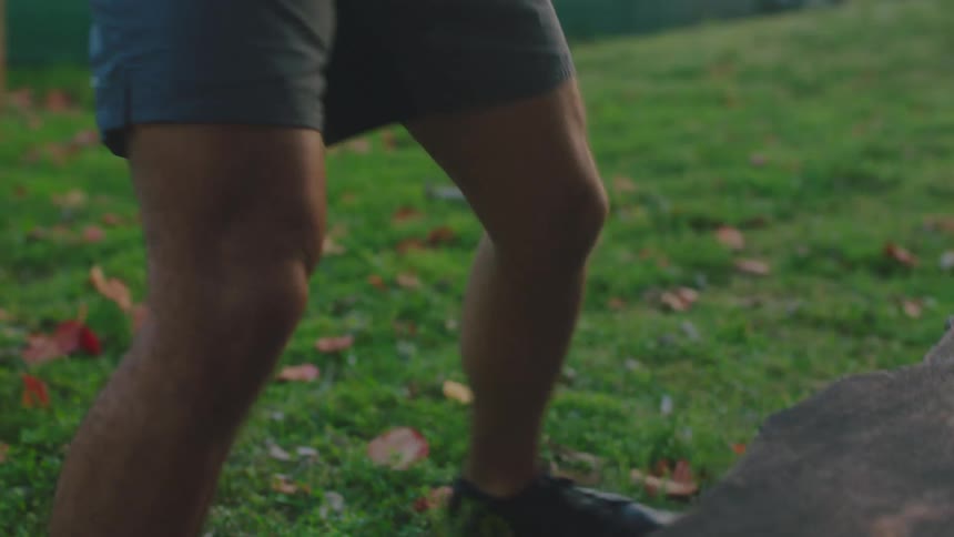 A man exercises by doing standing jumps onto a stone bench in a park