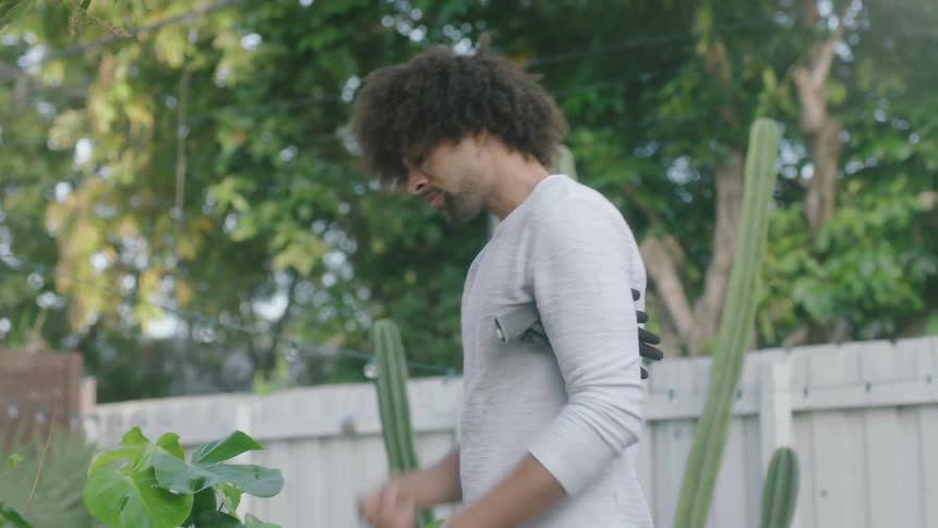 A man taking off gloves in a backyard with trees the sky and clouds in the background