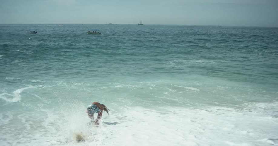 A young man runs down the beach with his surfboard and jumps on it as he enters the water