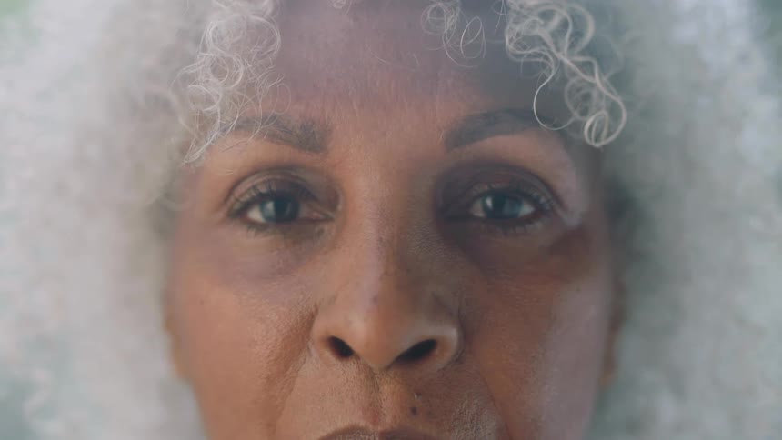 A black woman with curly white hair opens her eyes