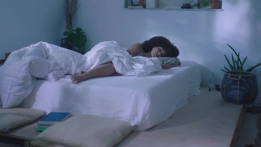 Woman sleeping half covered in bed sheets sleeping in a bed on a dimly lit room