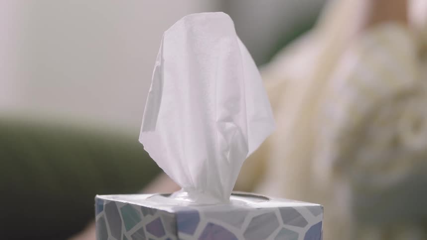 A woman takes a tissue out of a box