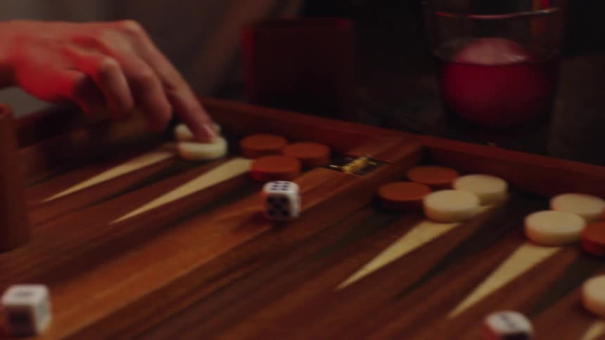 A person rolls the dice and moves during a backgammon game played by candle light