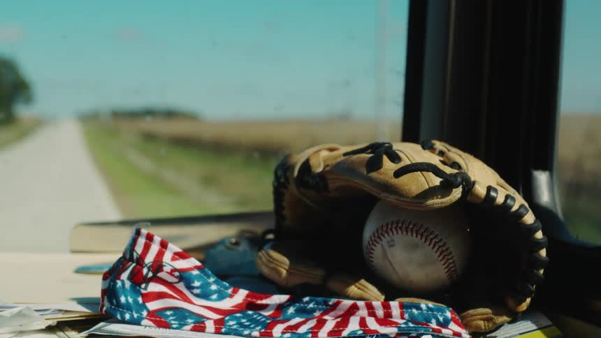 A vehicle with a baseball and mitt on the dashboard drives past a cornfield