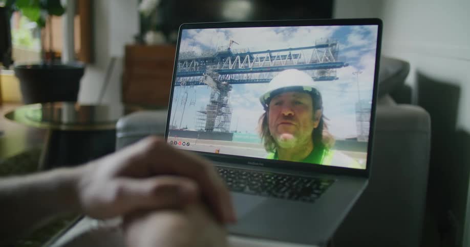 A construction worker wearing hardhat on a video call in a laptop with someone at home