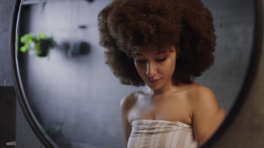 Brunette woman with frizzy hair looks in the mirror and washes her face in the bathroom