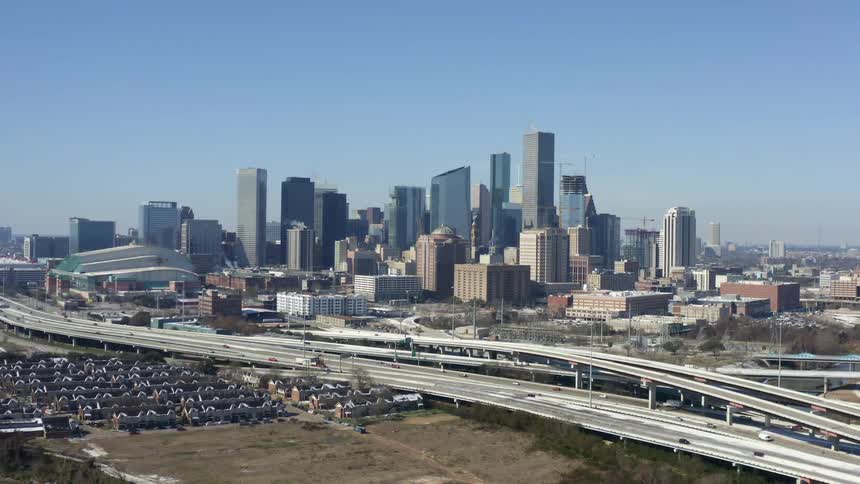 An aerial view of vehicles driving on a street in front of the Houston skyline