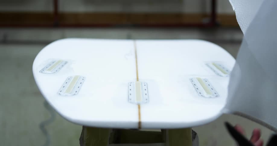 A man puts material over a surfboard he is making