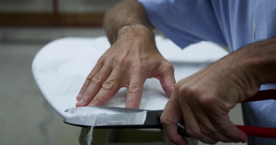 A man using scissors to trim the eges of a surfboard in a workshop