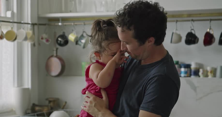 A dad kisses his daughter and hugs her as she rubs her eyes