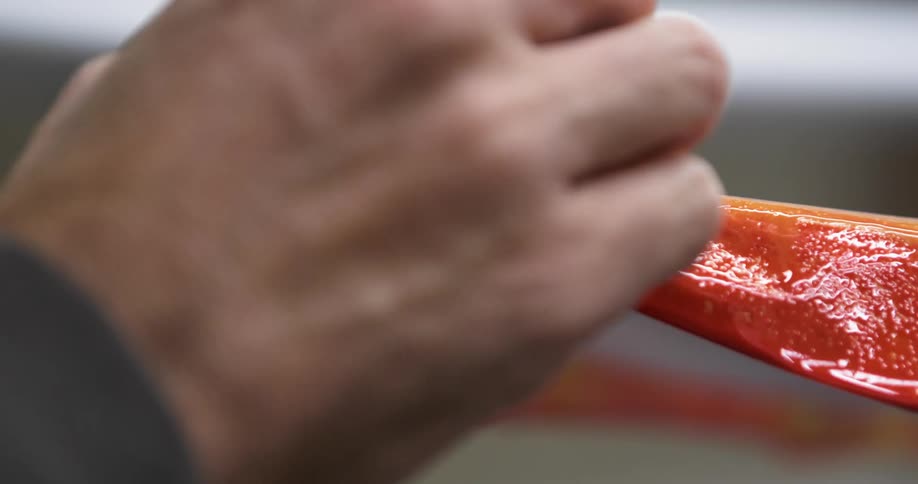 A man peels red and orange plastic off the tip of a surfboard