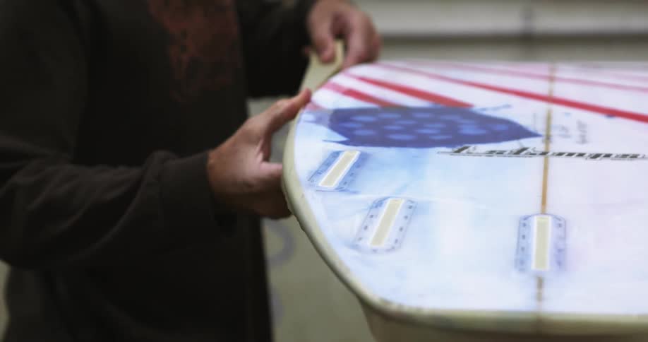 A man taping the border of a surfboard in a workshop