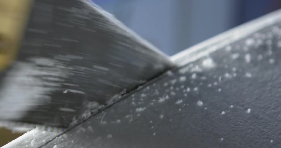 A hand holding a saw with a yellow handle cuts off the edge trimming of a piece of a gray piece of plastic