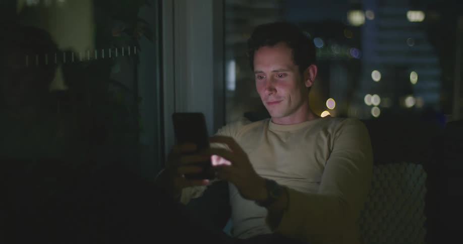 Man sitting next to corner window at home scrolling on social media on phone