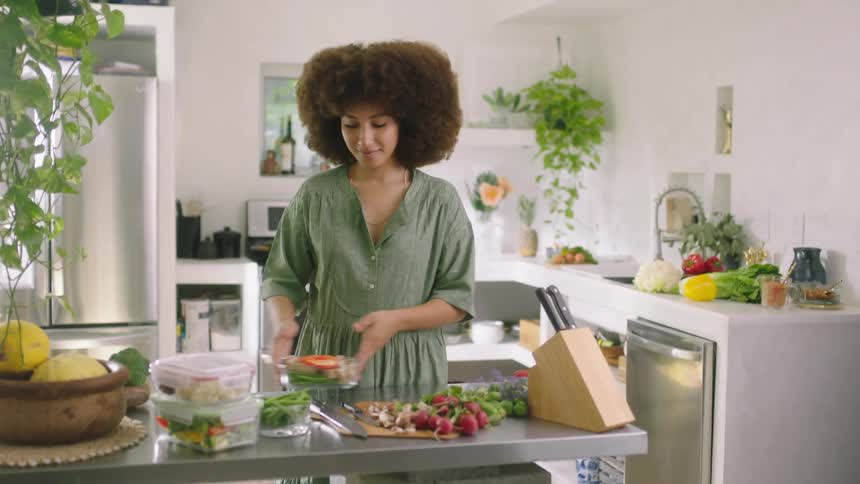 Young woman with an afro wearing a green dress preparing food in the kitchen counter top at home