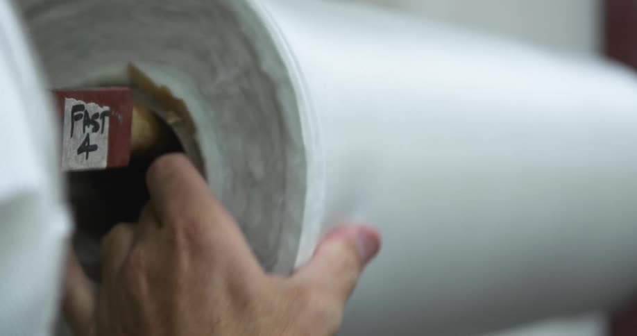 A man turning a roll of fabric on a shelf