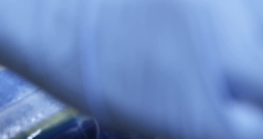 A hand wearing a blue latex glove spreads blue paint across the surface of a board as some drips off to the side